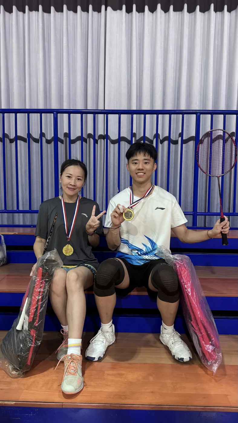 Wuqian Tang and his doubles partner holding their first-place medals and rackets at the 2025 NTHU Interdepartmental Cup badminton competition.